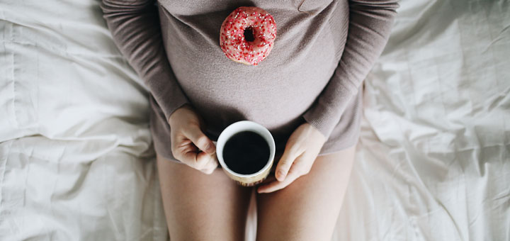 Schwangere Frau mit Donut und Tee auf einem Bett