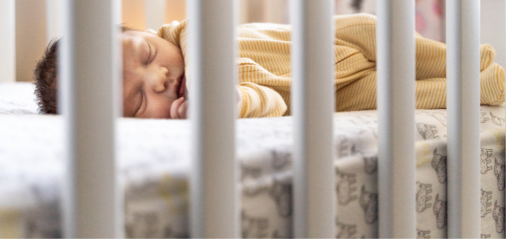 Baby schläft im Gitterbett auf einer Babymatratze.